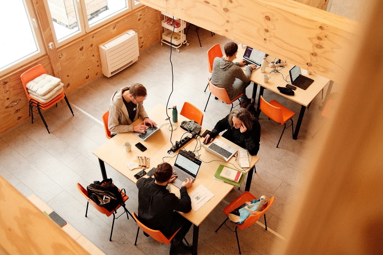 Offener, heller Arbeitsraum mit mehreren Menschen an Laptops in konzentrierter, gemeinschaftlicher Atmosphäre.